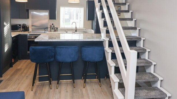 Una cocina moderna con una isla central, taburetes de bar y una escalera que incorpora un rascador para gatos.