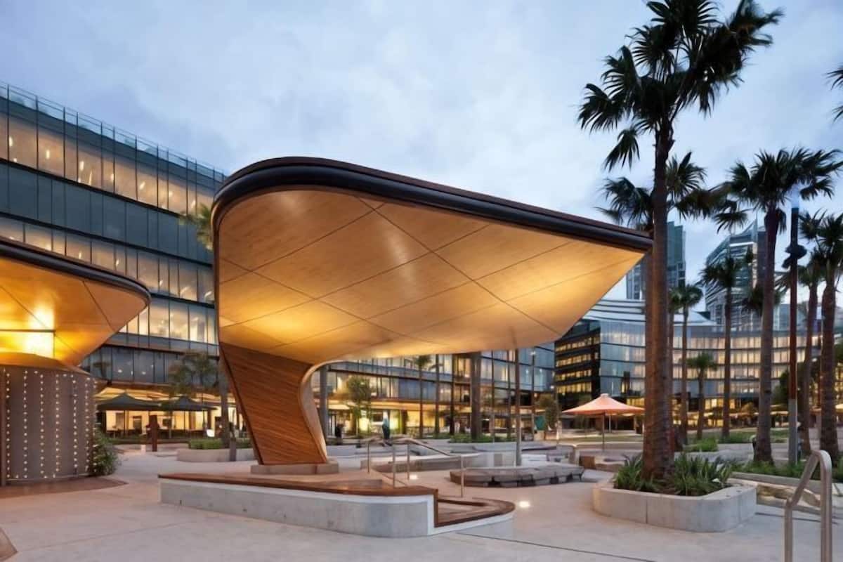 A modern building with a unique curved roof structure, surrounded by palm trees and a well-lit plaza.