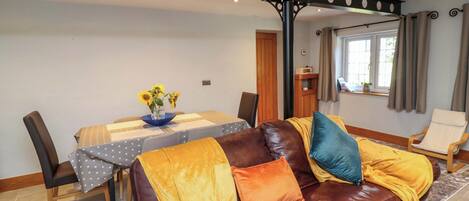 A living room with a brown leather sofa, a dining table with a polka dot tablecloth, and a vase with sunflowers.