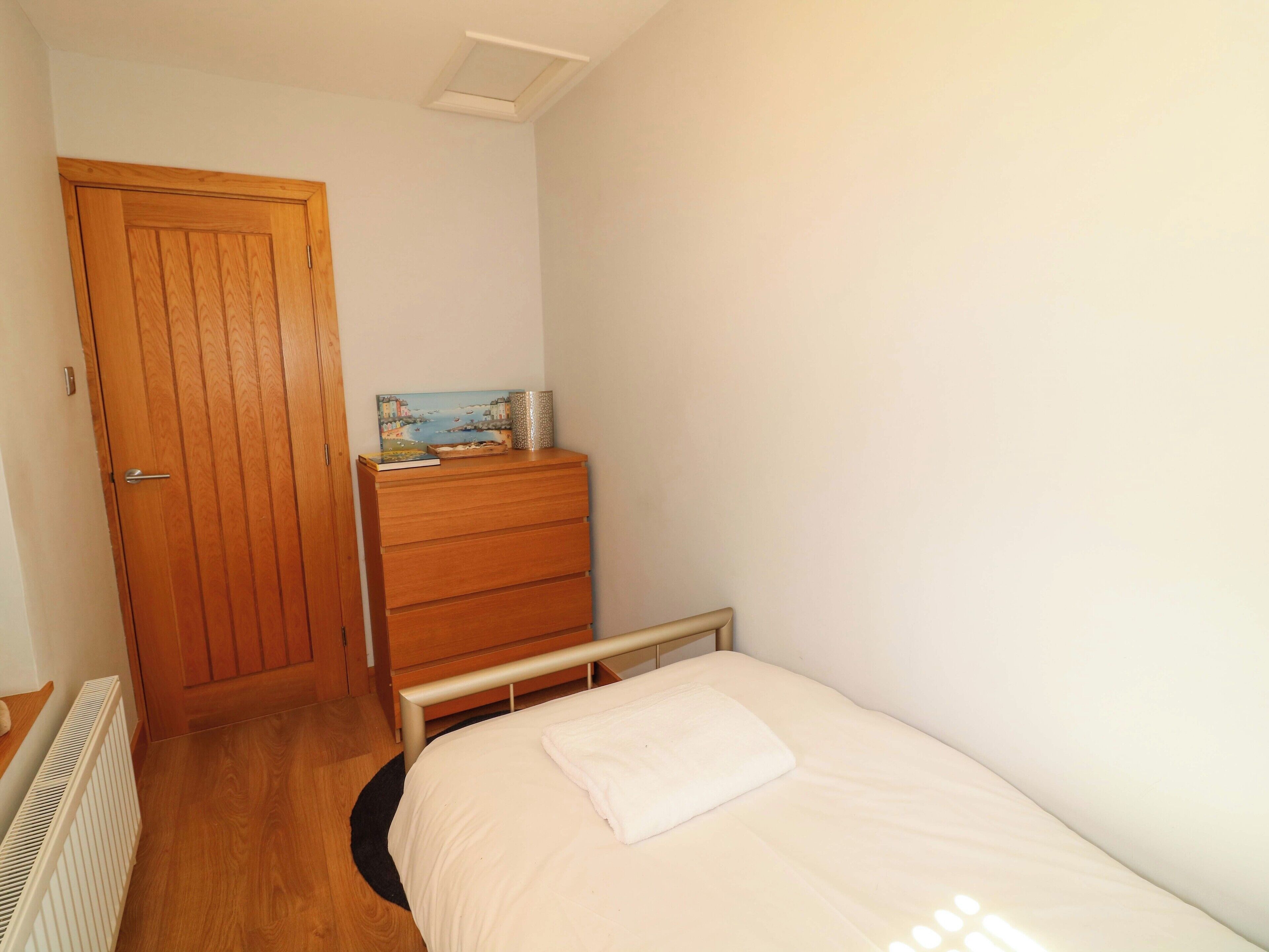 A bedroom with a wooden door, a dresser, a bed with a white pillow, and a radiator.