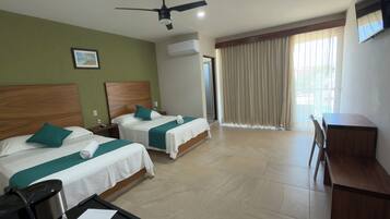 A hotel room with two beds, a desk, a chair, a ceiling fan, an air conditioning unit, and a window with curtains.