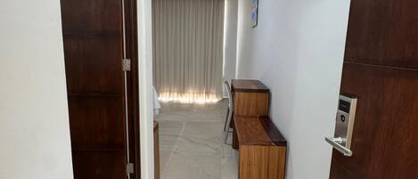 A hallway with a wooden door, a bench, and a desk.