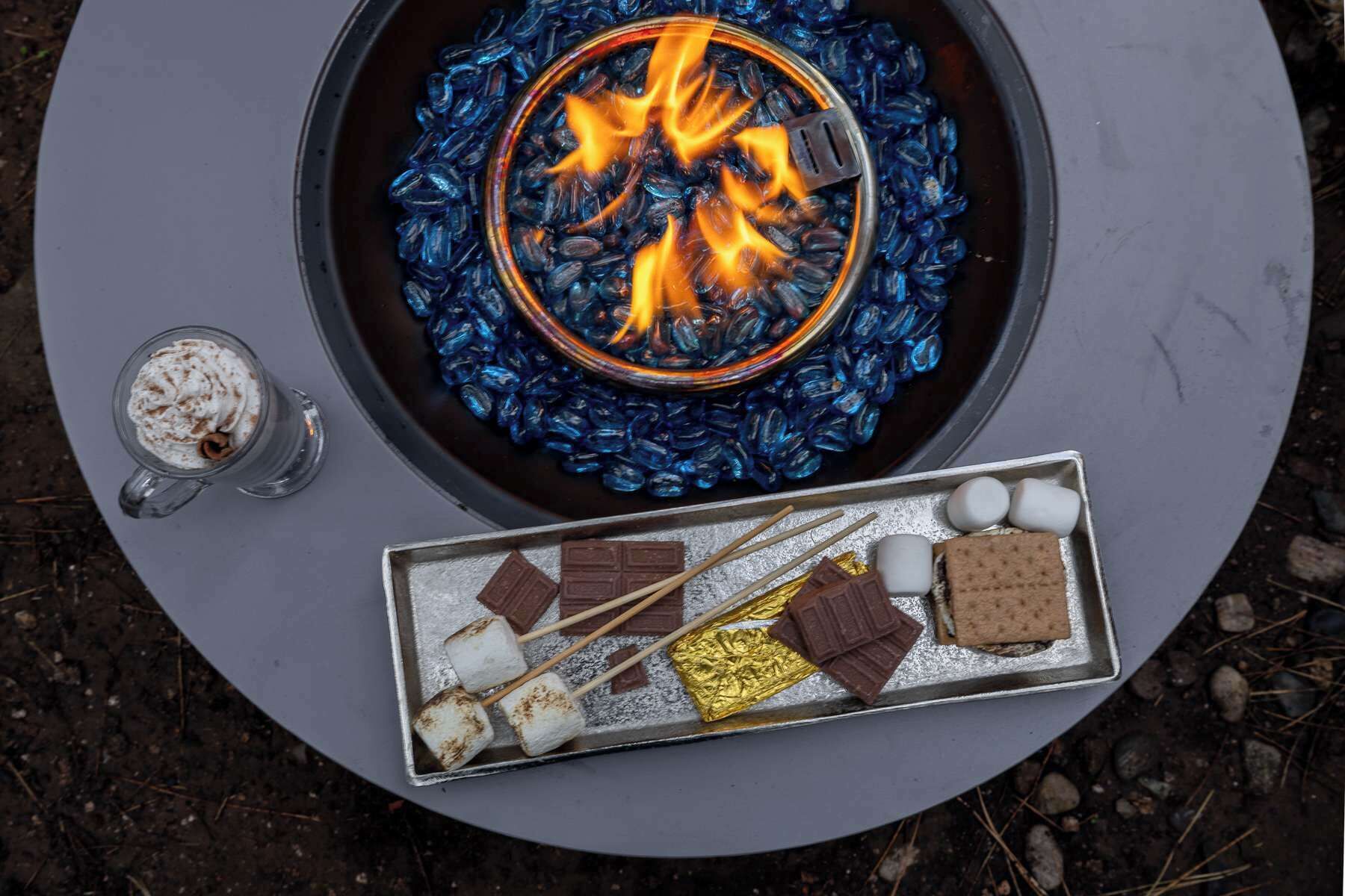 A campfire with a metal tray of marshmallows, chocolate, and graham crackers.