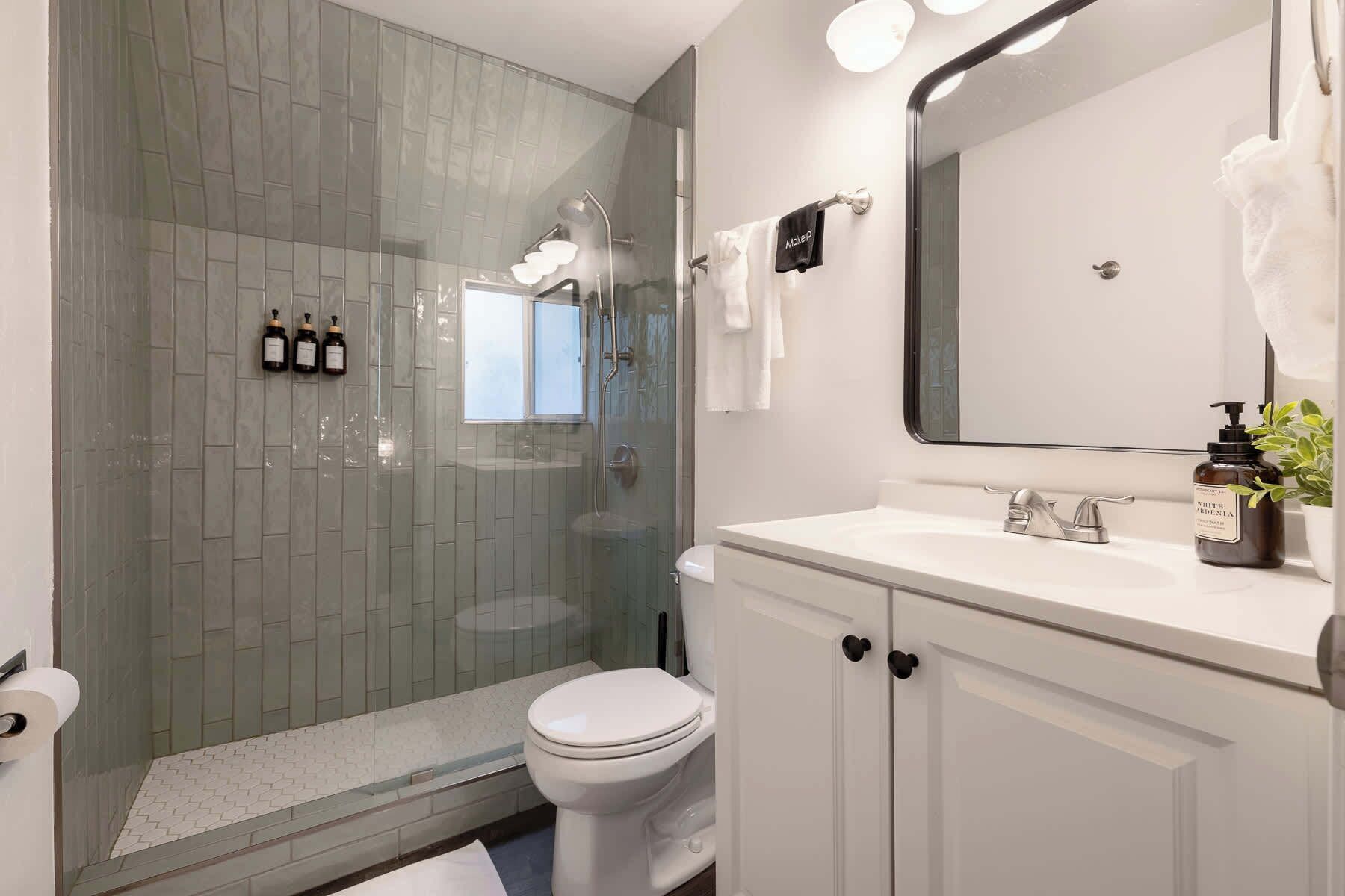A modern bathroom with a glass shower enclosure, a white toilet, a sink with a mirror, and toiletries on the countertop.