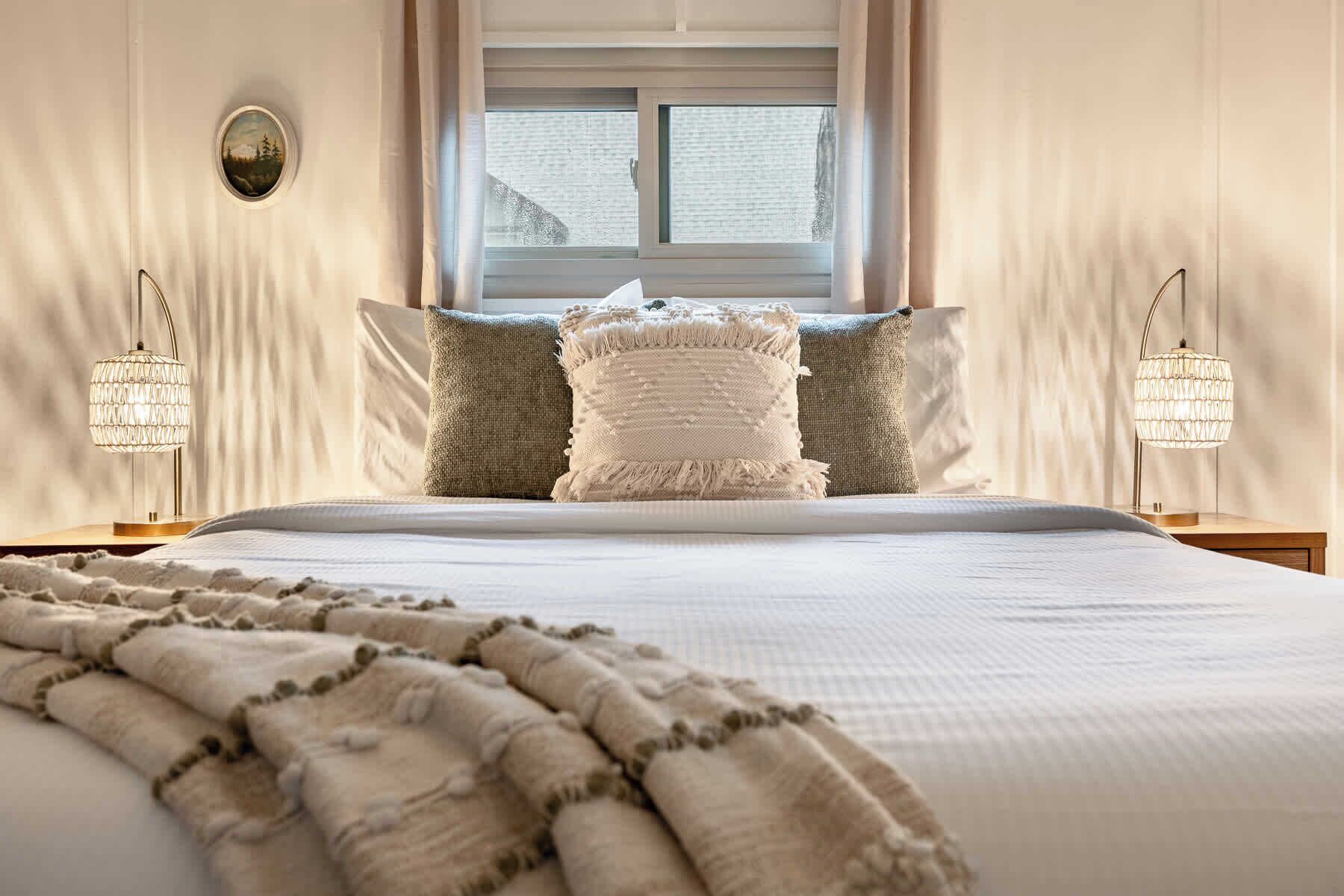 Un letto con un copriletto bianco, due cuscini e una coperta. Due abat-jour con un design simile al cristallo.