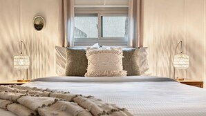 Una cama con edredón blanco, dos almohadas y una manta. Hay dos lámparas de noche con un diseño similar al cristal.