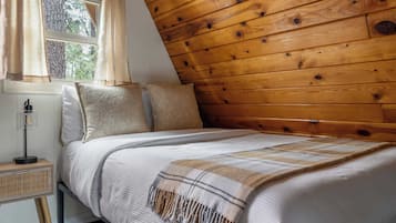 A bedroom with a sloped wooden ceiling, a bed with a striped blanket, and a bedside lamp.