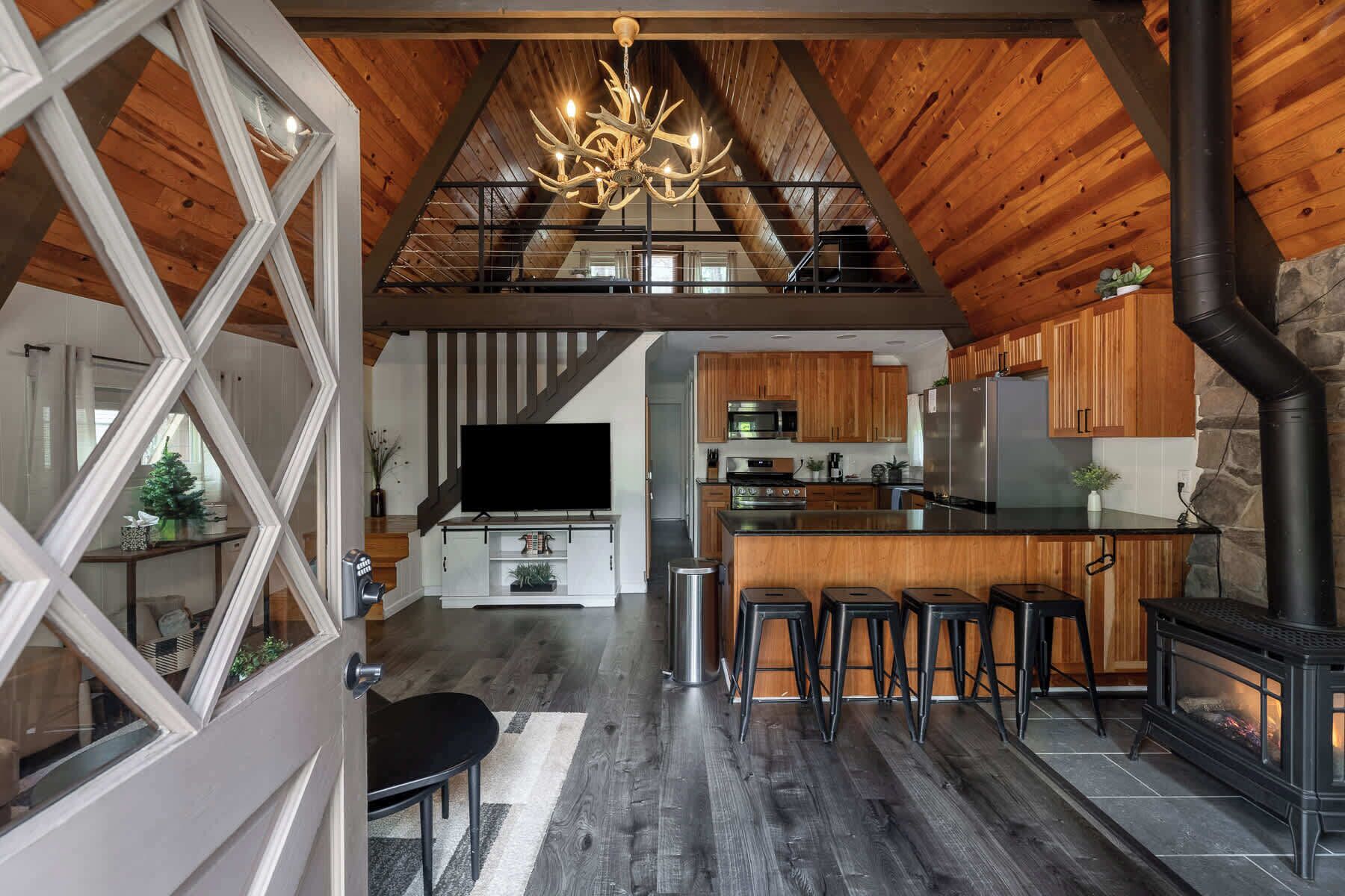 Een ruime leefruimte in loftstijl met een hoge plafond, houten balken, een open haard en een moderne keuken.
