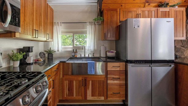 Cocina moderna con armarios de madera, refrigerador de acero inoxidable, estufa a gas y ventana con vista a follaje.
