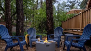 Una terraza con sillas Adirondack azules, una fogata y barandilla de madera.