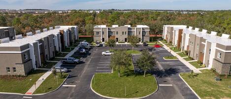 A modern apartment complex with a central courtyard, parking, and a view of the surrounding area.