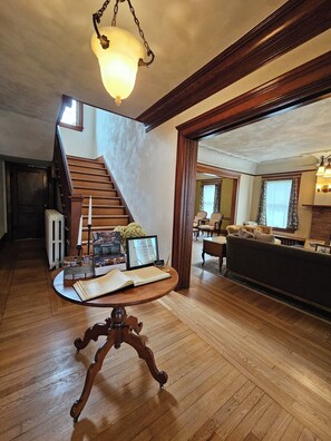 A spacious living area with a wooden staircase, a round table with a book and certificates, and a cozy seating area with a sofa and chairs. - Historic, 4-bedroom house in charming Hartford (Hartford)