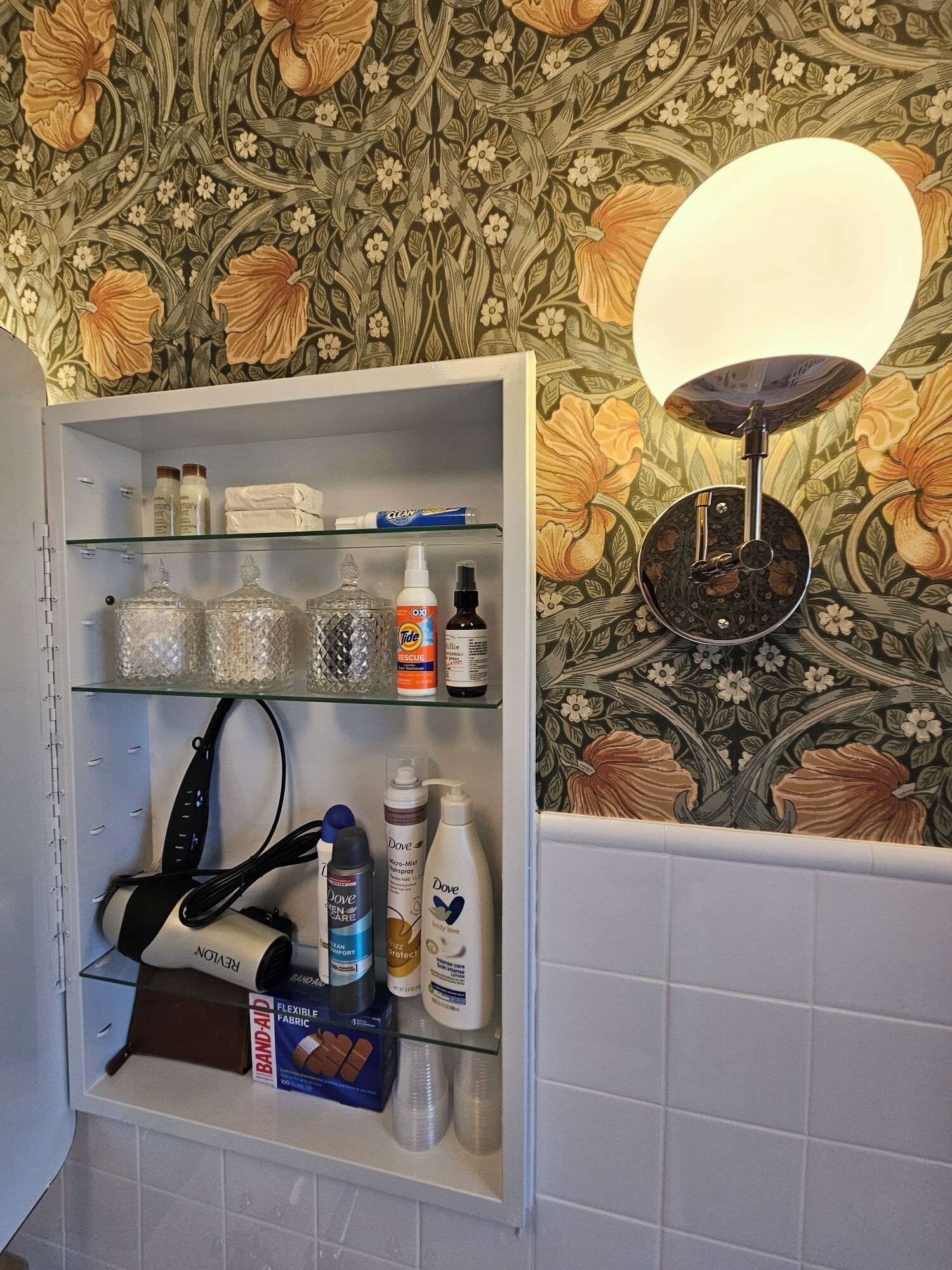 Une salle de bain avec un meuble-lavabo, un miroir et un mur recouvert d’un papier peint à motifs floraux.