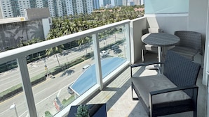 A balcony with a view of a cityscape, a glass table with a plant, and wicker furniture.