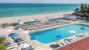A resort pool area with lounge chairs and umbrellas, a beach, and a clear view of the ocean.
