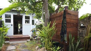 Een houten constructie met een bank en een handdoek die hangt, omringd door tropische planten en een kiezelpad.