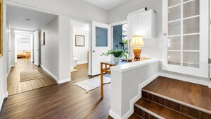 A hallway with wooden flooring, white walls, and a staircase leading to an upper level.