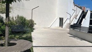 Un espace extérieur moderne avec un chemin en béton, un banc en bois et un escalier menant à un niveau supérieur.