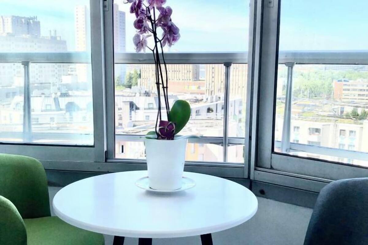Una habitación con una mesa redonda blanca, una orquídea en maceta y vistas de un paisaje urbano a través de amplias ventanas.