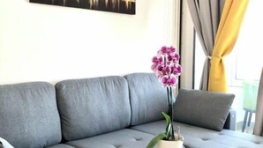Un canapé gris agrémenté d’une orchidée en pot, une petite table ronde et une fenêtre avec des rideaux.