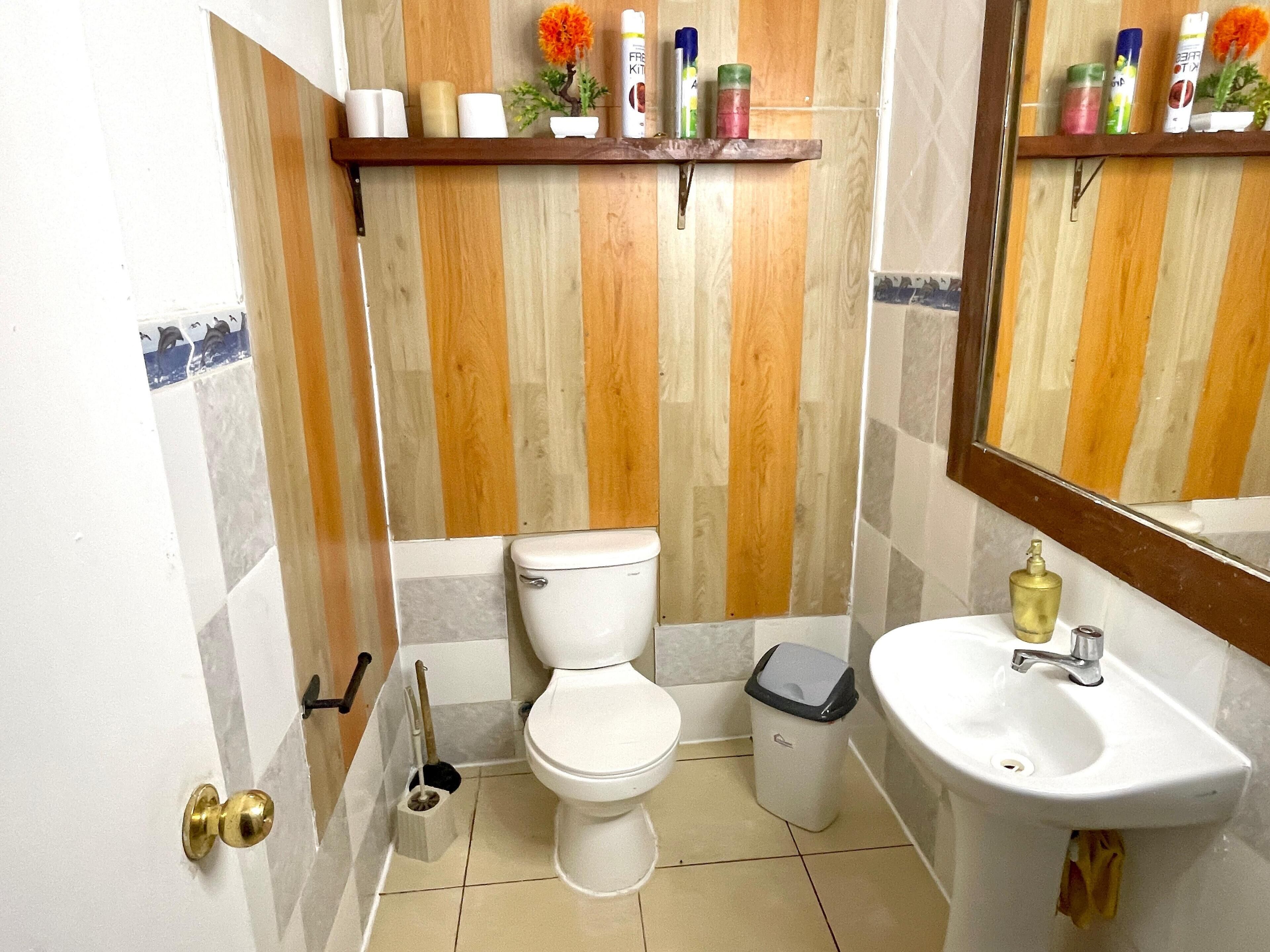 Un baño con inodoro, lavabo y estante con artículos de aseo.