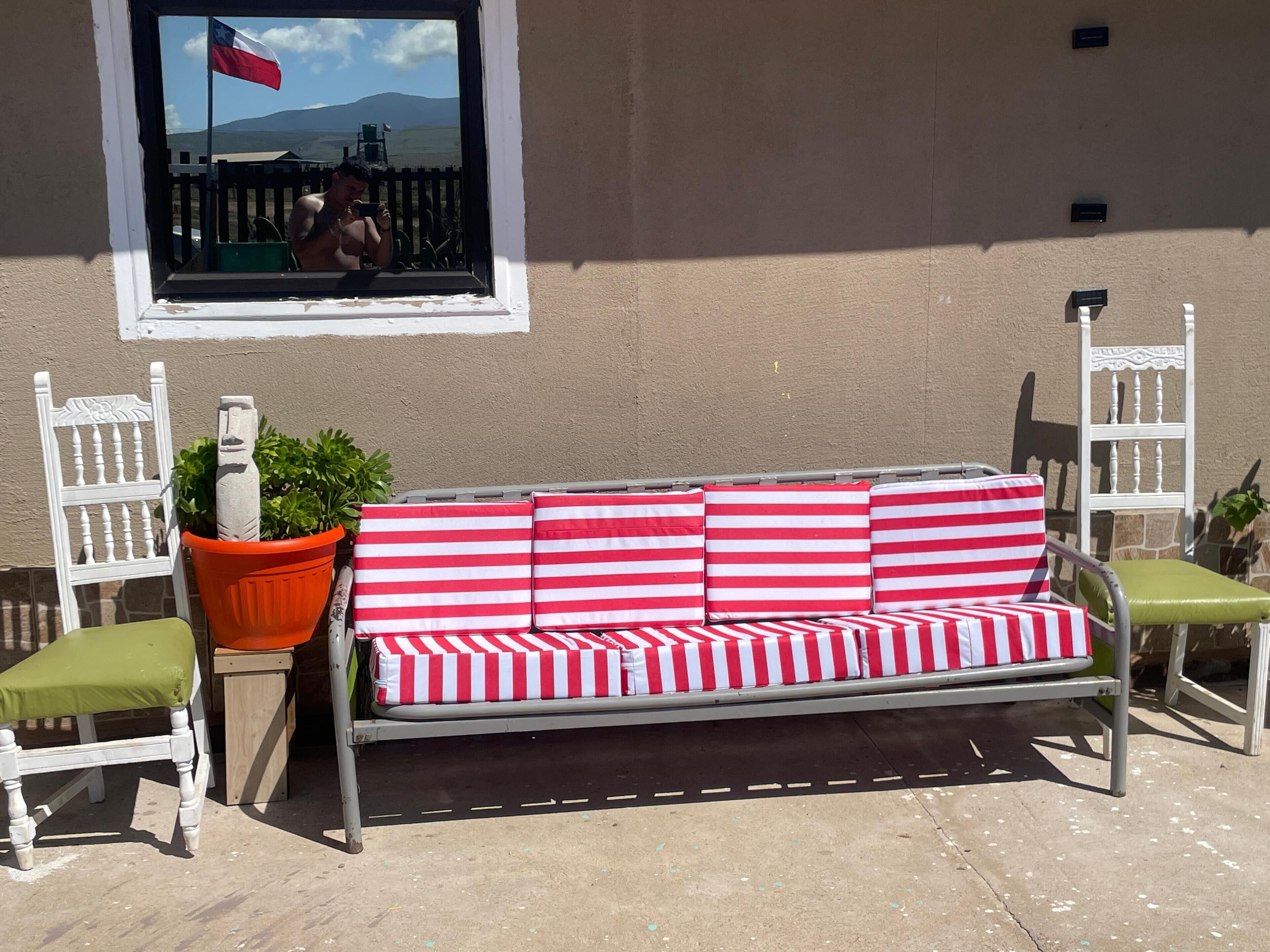 A metal outdoor sofa with red and white striped cushions, two white chairs with green cushions, and a potted plant.