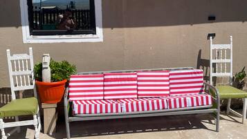 A metal outdoor sofa with red and white striped cushions, two white chairs with green cushions, and a potted plant.