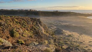 Un paisaje costero con terreno rocoso, vegetación escasa y una vista distante del mar.