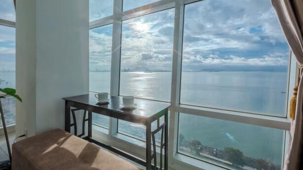 A room with large windows, a small table with a cup, and a plant. - Maritime Seaview Comfy Suite in Penang with TVbox.Pool.Wifi (George Town)