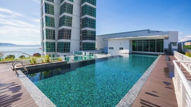 Um hotel moderno com piscina no terraço, um edifício grande com janelas refletoras e vista para o mar.