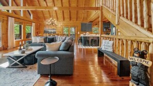 A spacious log cabin interior with a large living area, a dining area, and a staircase leading to a loft. - Rustic Cove: Views, Hot Tub, Theater & Game Room! (Sevierville)