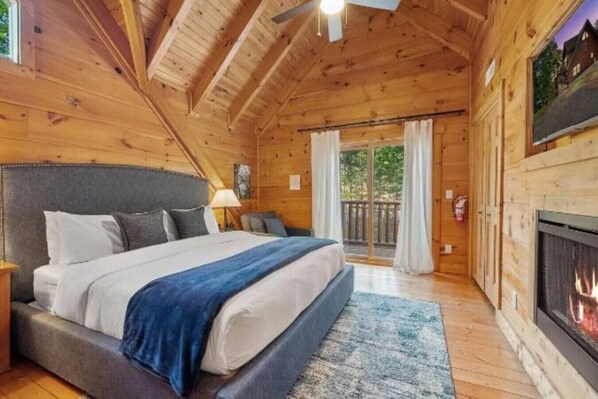 A cozy log cabin bedroom with a large bed, a fireplace, and a balcony with curtains.