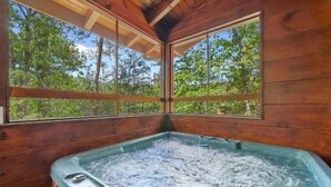 A wooden cabin with a hot tub and large windows offering a forest view. - Rustic Cove: Views, Hot Tub, Theater & Game Room! (Sevierville)