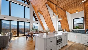 A spacious kitchen with a large island, wooden ceiling beams, and large windows offering a mountain view.