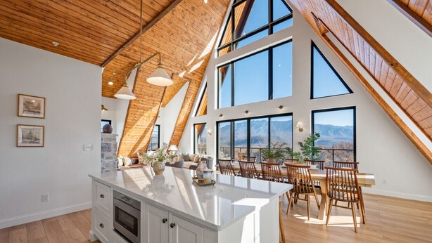 A spacious kitchen with a large island, wooden ceiling beams, and large windows offering a mountain view.