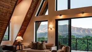 A spacious living area with a high ceiling, large windows, and a view of mountains.