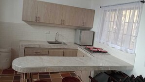 A kitchen with a marble countertop, wooden cabinets, a sink, a refrigerator, and a window with sheer curtains. - CASA DE CAMPO PRIVADA CON PISCINA (La Mesa)