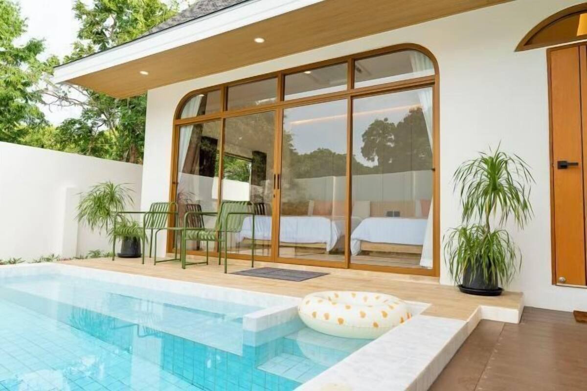 Zona de piscina moderna amb una sala envidriada, una piscina i seients exteriors.