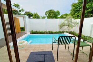 Una piscina con muelle de madera, una silla verde y una de metal.