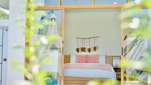 Une chambre à coucher avec un lit, un luminaire suspendu et une vue à travers une porte vitrée.