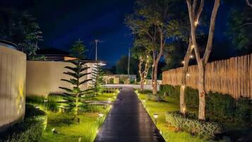 A nighttime pathway flanked by trees and illuminated by ground lights, leading to a building.
