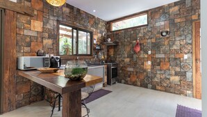 Una cocina con pared de piedra, una mesa de madera, un acuario, un microondas, una tetera y una estufa.