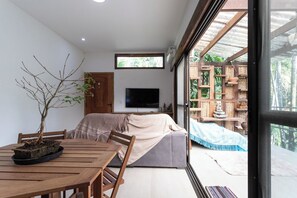 A modern interior with a wooden dining table, a sofa, a TV, and a large window offering a view of the outdoors. - Casa de Campo c Lareira Externa Rede e Lago (Rio de Janeiro)