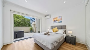 A bedroom with a bed, nightstand, and a view through a sliding door to an outdoor area. - Luxe Living Terrace by The Star - Luxury in Sydney (Pyrmont)