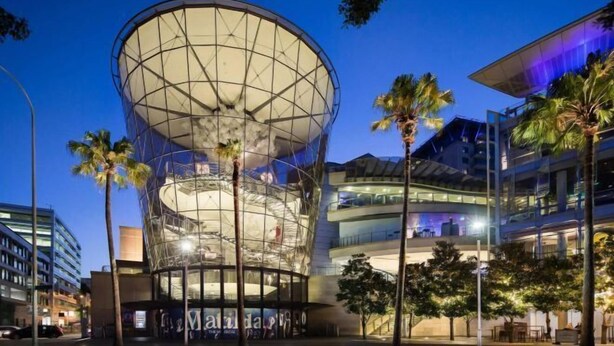 A modern building with a large circular glass structure, surrounded by palm trees and other buildings. - Luxe Living Terrace by The Star - Luxury in Sydney (Pyrmont)