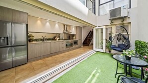 A modern kitchen with stainless steel appliances, a dining area with a glass table, and a hanging chair. - Luxe Living Terrace by The Star - Luxury in Sydney (Pyrmont)