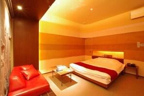 A modern hotel room with a bed, a red sofa, a small table, and a nightstand. - Blue Hotel Nagi-Adult Only (Otaru)