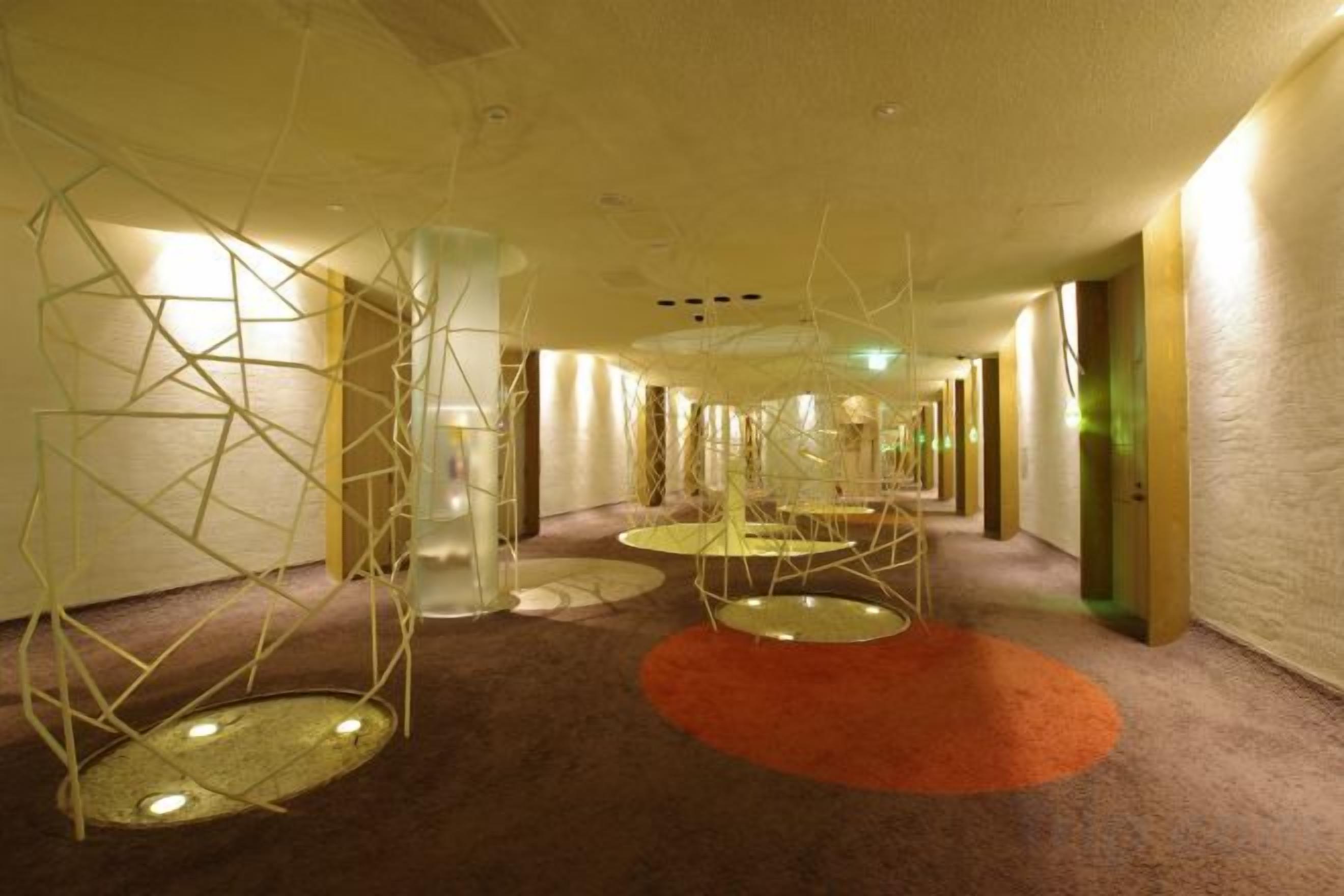 Een hotelgang met een modern design, met geometrische lampen en een vloerkleed.