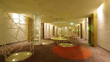 Een hotelgang met een modern design, met geometrische lampen en een vloerkleed.