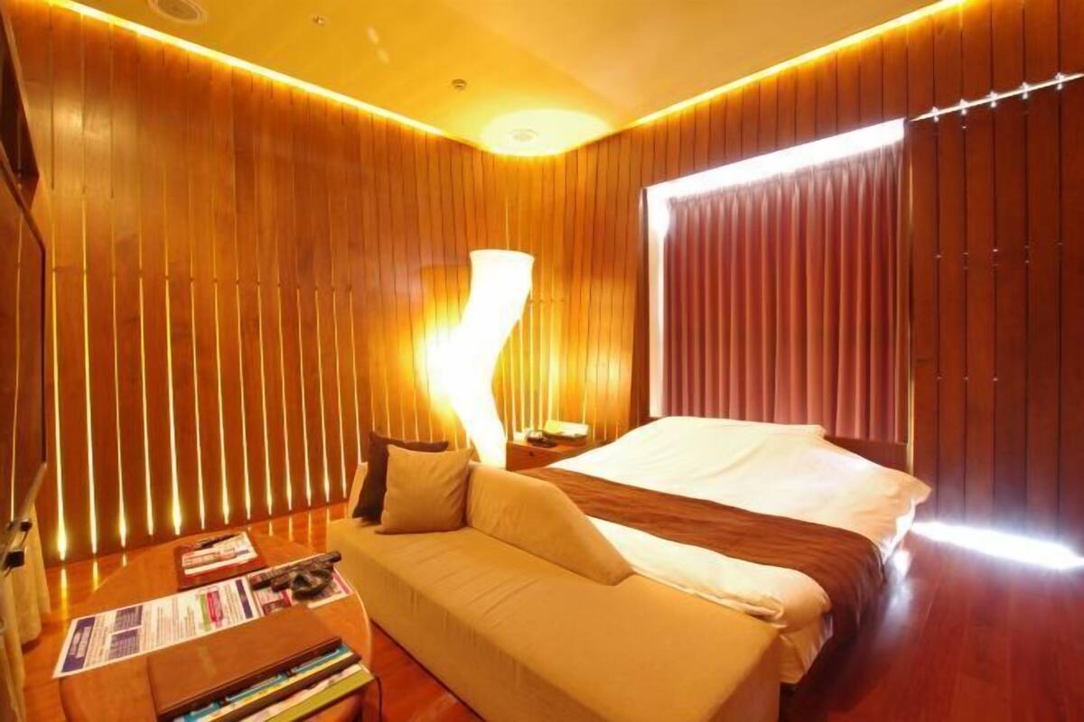 A hotel room with a bed, a sofa, a nightstand, and a lamp.